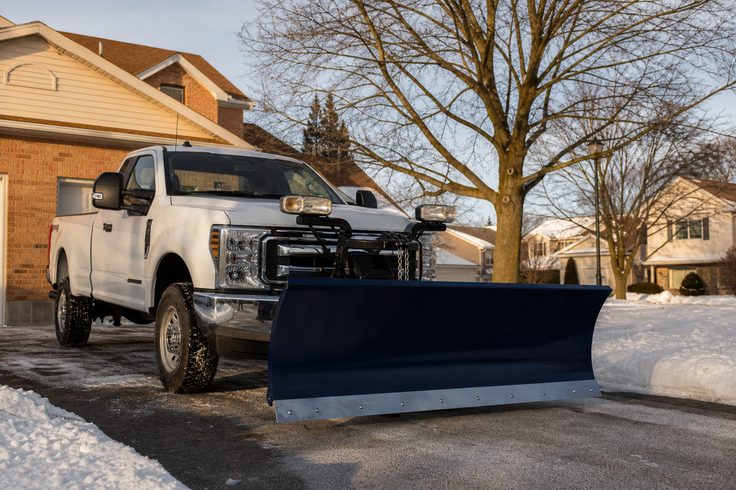 Snow removal equipment parked at the edge of a cleared residential driveway